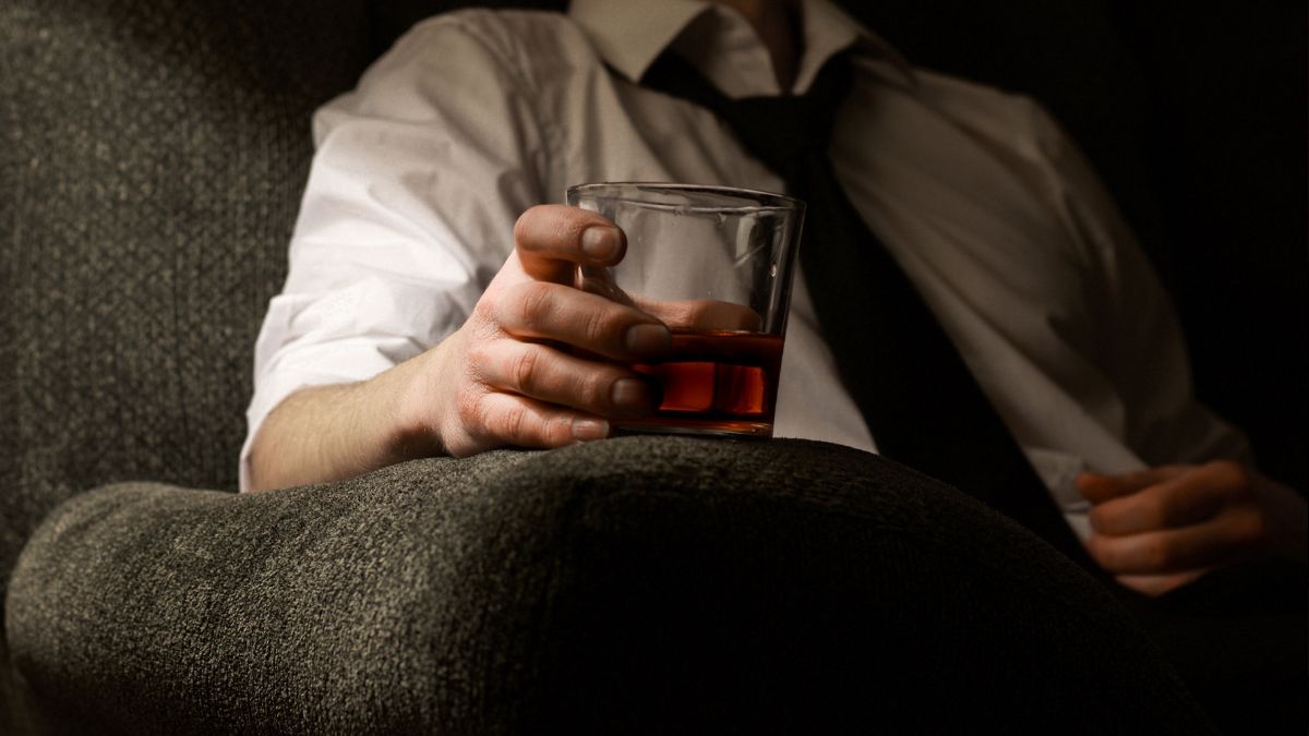 man holding a whisky sitting on a couch